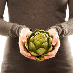 Mid section of a woman with an artichoke in her hands isolated o